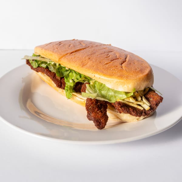 Cuban sandwich with fried pork, lettuce, and potato sticks on a white plate.