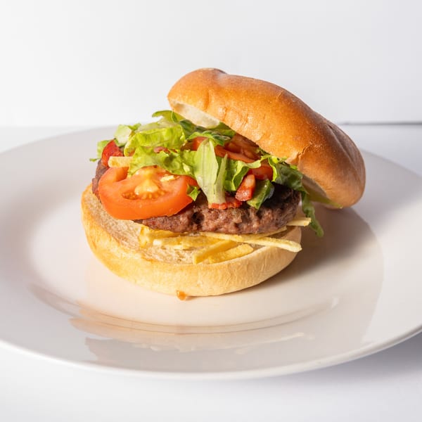 A Cuban-style burger on a white plate, topped with lettuce, tomato, and shoestring fries.