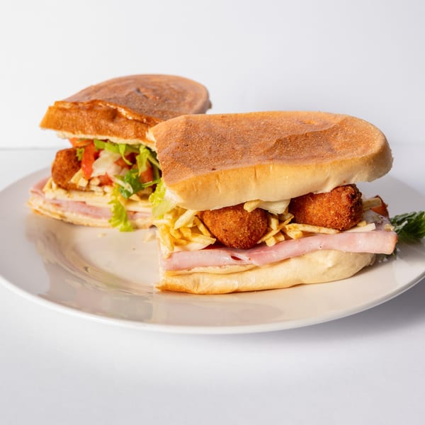 Two Mervis' Cafe Cuban sandwiches with ham, cheese, croquettes, and fries on a white plate.