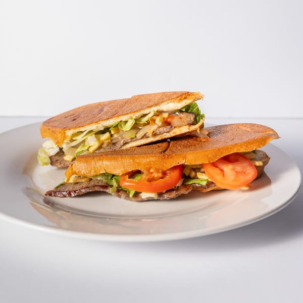 Two halves of a Cuban steak sandwich with lettuce, tomatoes, and fries on a white plate.