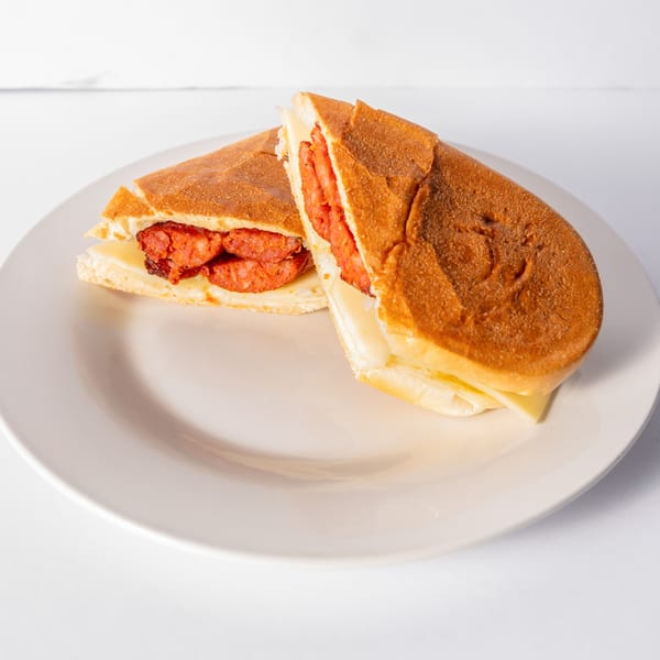 Two halves of a Cuban sandwich with chorizo and cheese on a white plate.