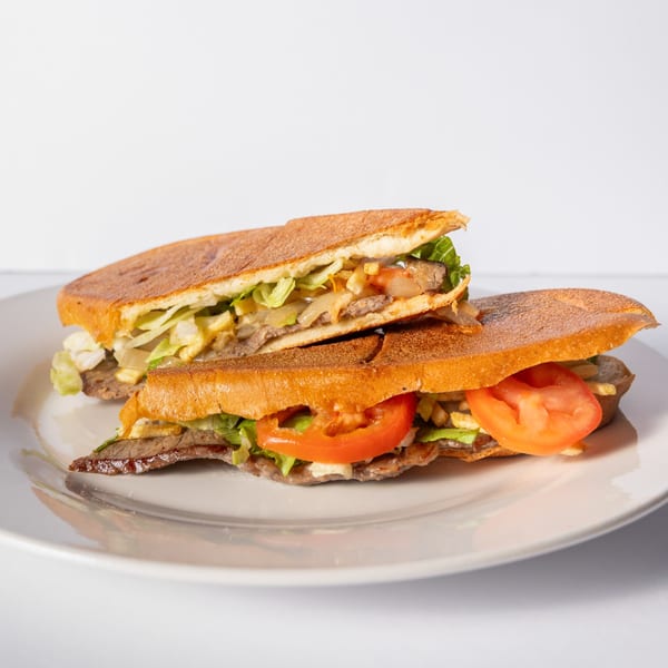 Two halves of a Cuban steak sandwich with lettuce, tomatoes, and fries on a white plate.